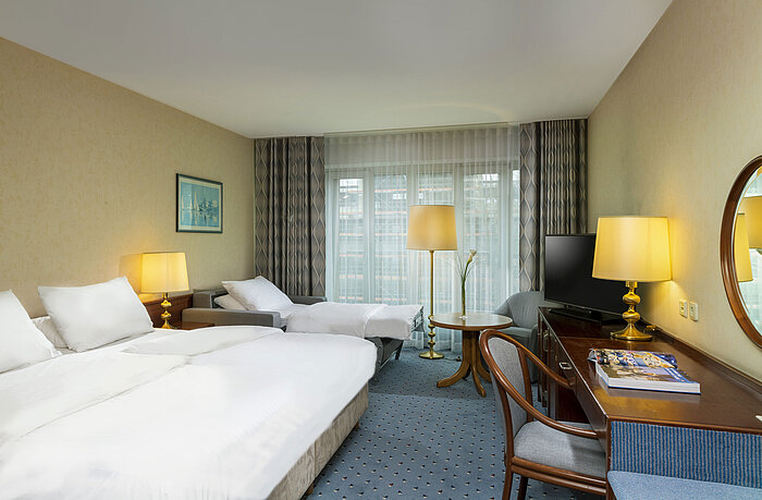 Helles Familienzimmer im Maritim Hotel Köln mit Doppelbett, Schreibtisch, Fernseher,Sesseln und großen Fenstern mit Vorhängen