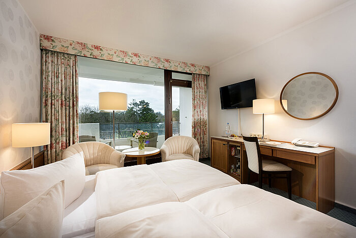 Classic Zimmer im Maritim Seehotel Timmendorfer Strand mit Balkon, Doppelbett, Sitzbereich, TV und Schreibtisch.