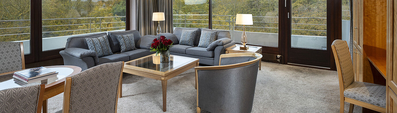 Wohnbereich der Grand Suite im Maritim Hotel Kiel mit großzügigen Fenstern, stilvoller Einrichtung und Blick ins Grüne.