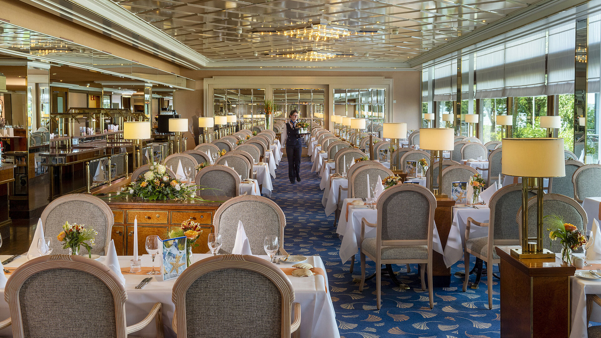 Großes, elegantes Restaurant mit langen, gedeckten Tischen, Kronleuchtern und Blumenarrangements für gehobenes Speisen.