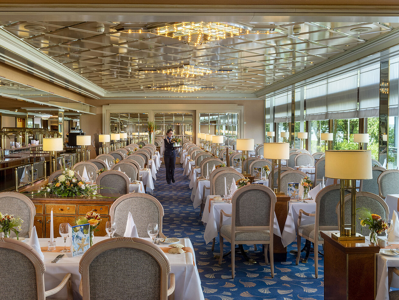 Großes, elegantes Restaurant mit langen, gedeckten Tischen, Kronleuchtern und Blumenarrangements für gehobenes Speisen.