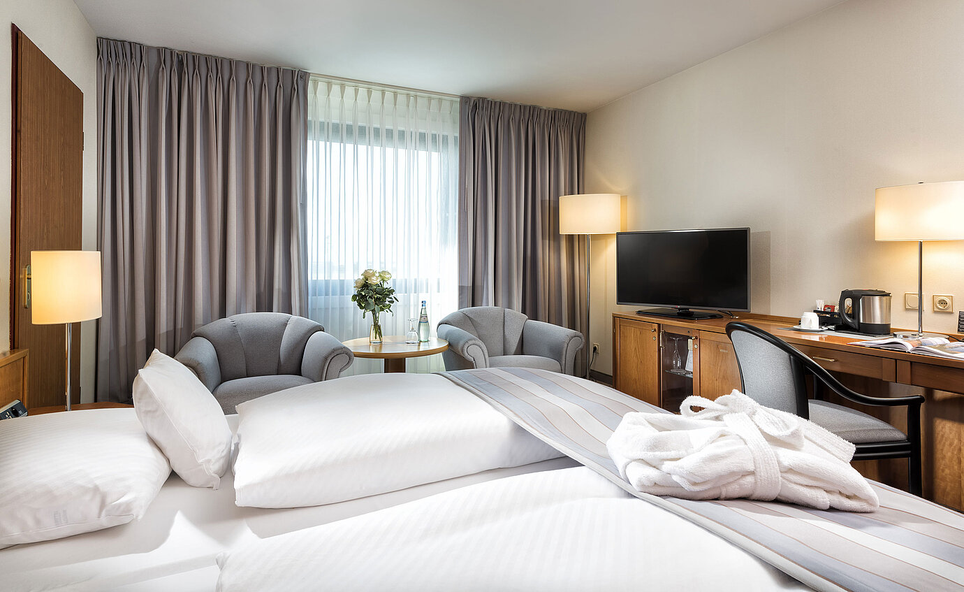 Superior Doppelzimmer mit stilvoller Einrichtung, gemütlichem Sitzbereich, Wasserflaschen und einem Bademantel auf dem Bett.