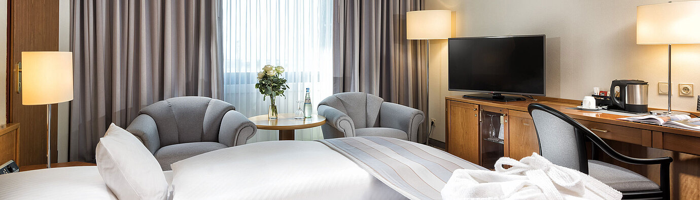 Superior Doppelzimmer mit stilvoller Einrichtung, gemütlichem Sitzbereich, Wasserflaschen und einem Bademantel auf dem Bett.