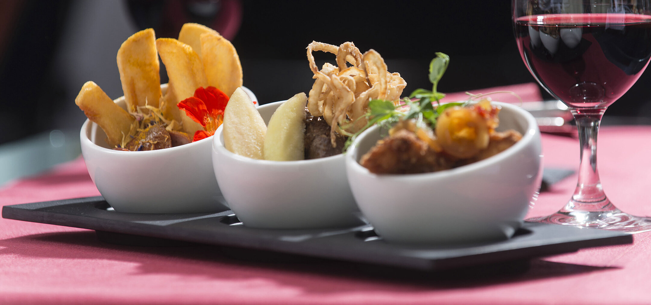 Nahaufnahme von Tapas im Maritim proArte Hotel Berlin, mit verschiedenen Köstlichkeiten und einem Glas Rotwein im Hintergrund