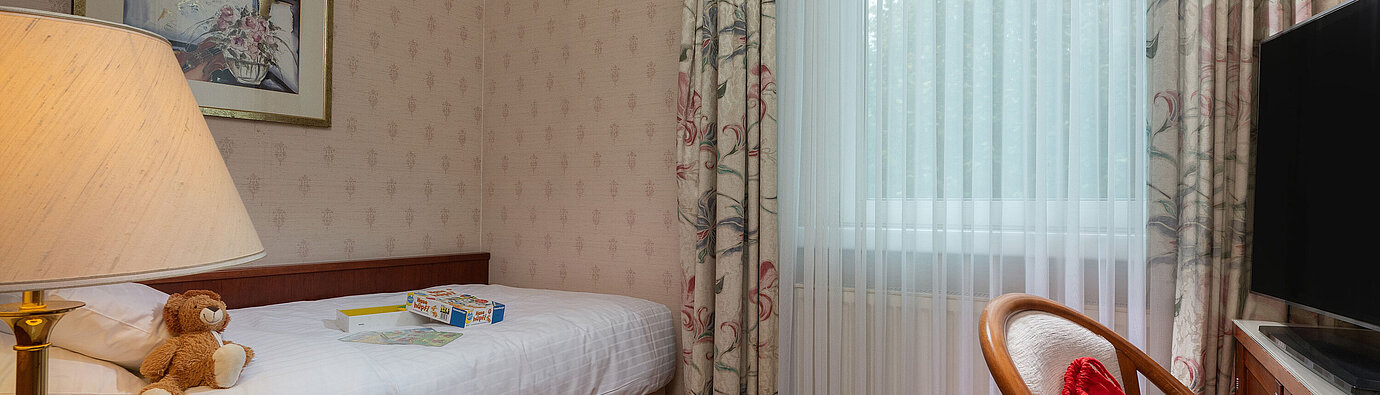 Comfort Familienzimmer Comfort Familienzimmer mit Einzelbett, Spielzeug, Sitzbereich und großer Fensterfront für einen gemütlichen Aufenthalt.