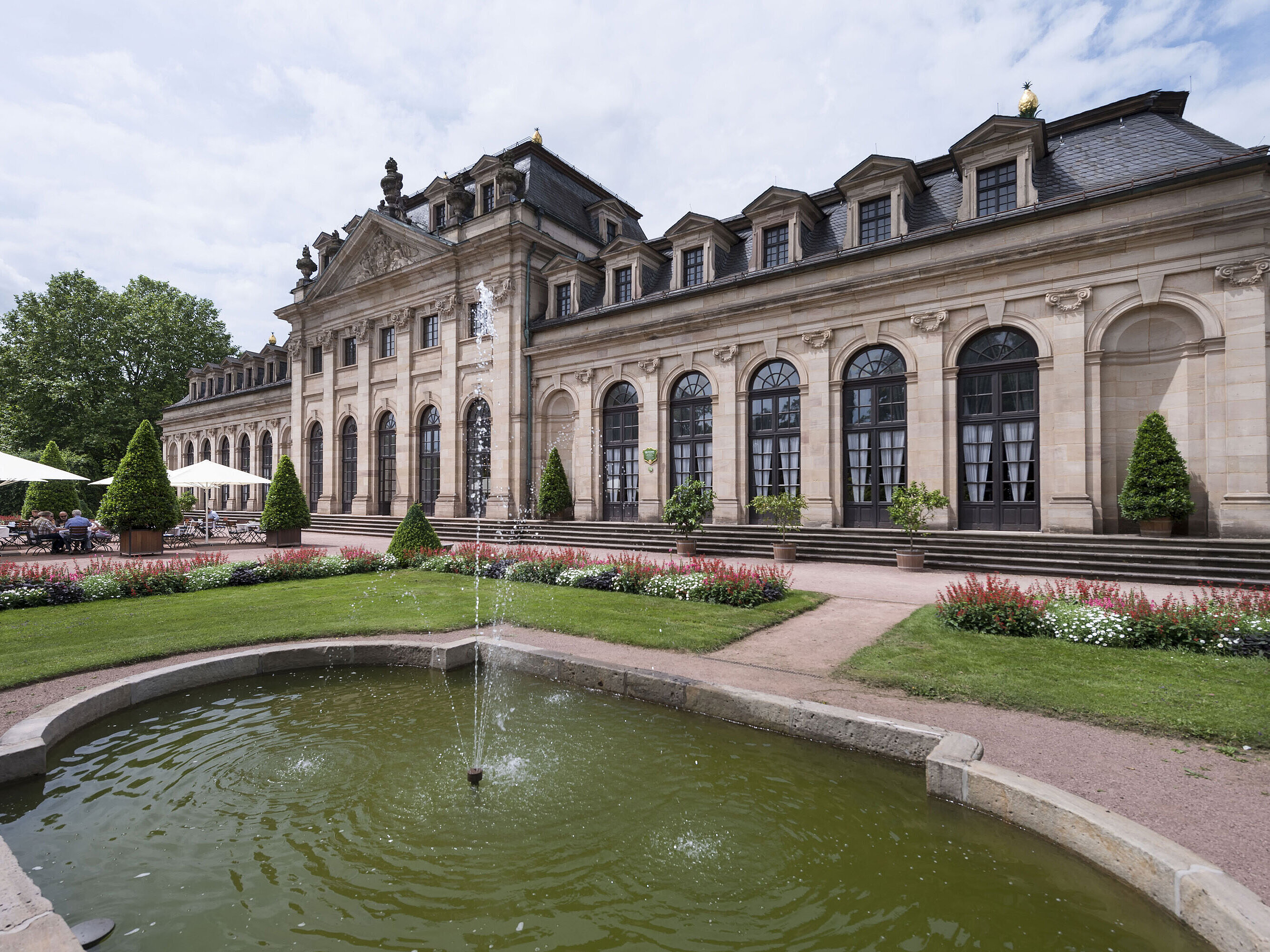 Die barocke Orangerie Fulda mit Terrasse, gepflegtem Garten und historischem Springbrunnen im Vordergrund.