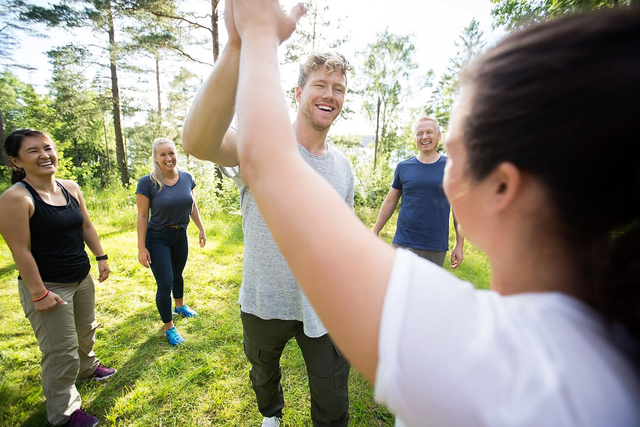 © Tyler Olsen AdobeStock.com Gruppe von Erwachsenen im Freien beim Teambuilding, High-Five im Grünen bei sonnigem Wetter