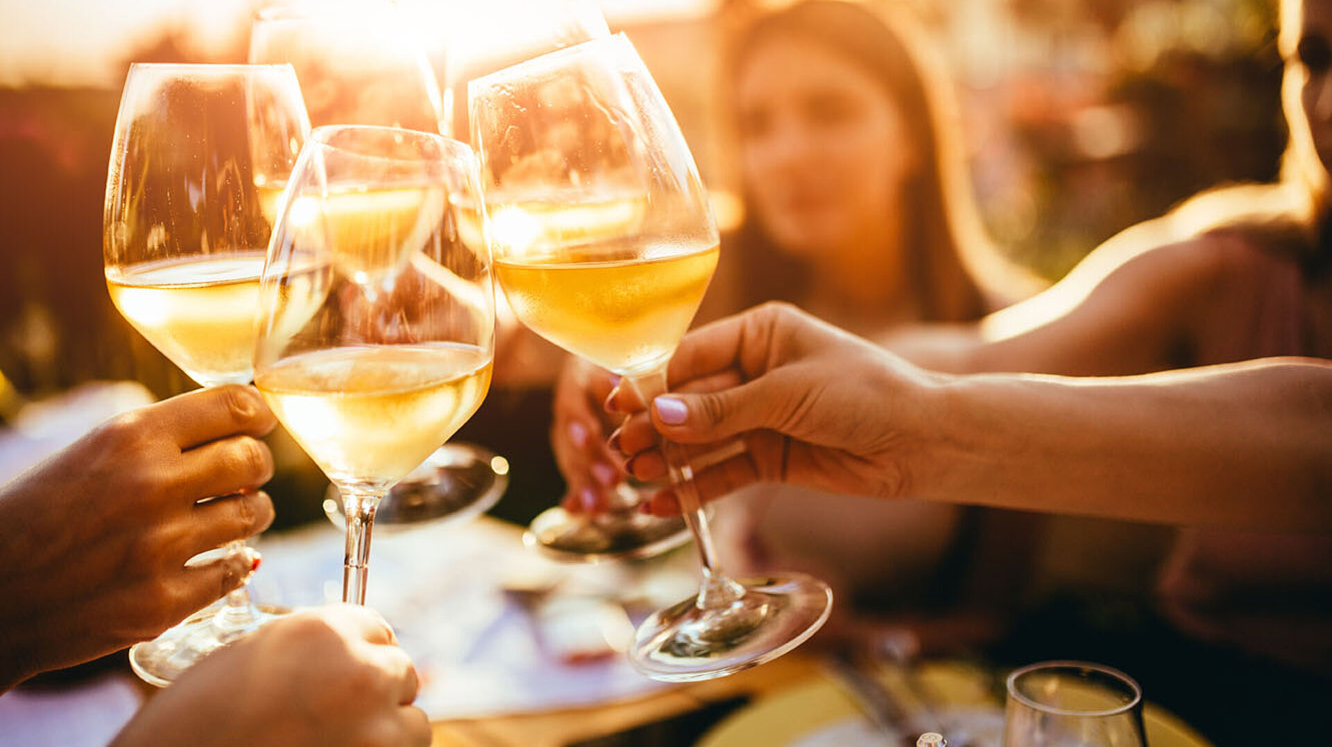 Freunde stoßen mit Weingläsern an und genießen einen gemeinsamen Abend bei Sonnenuntergang