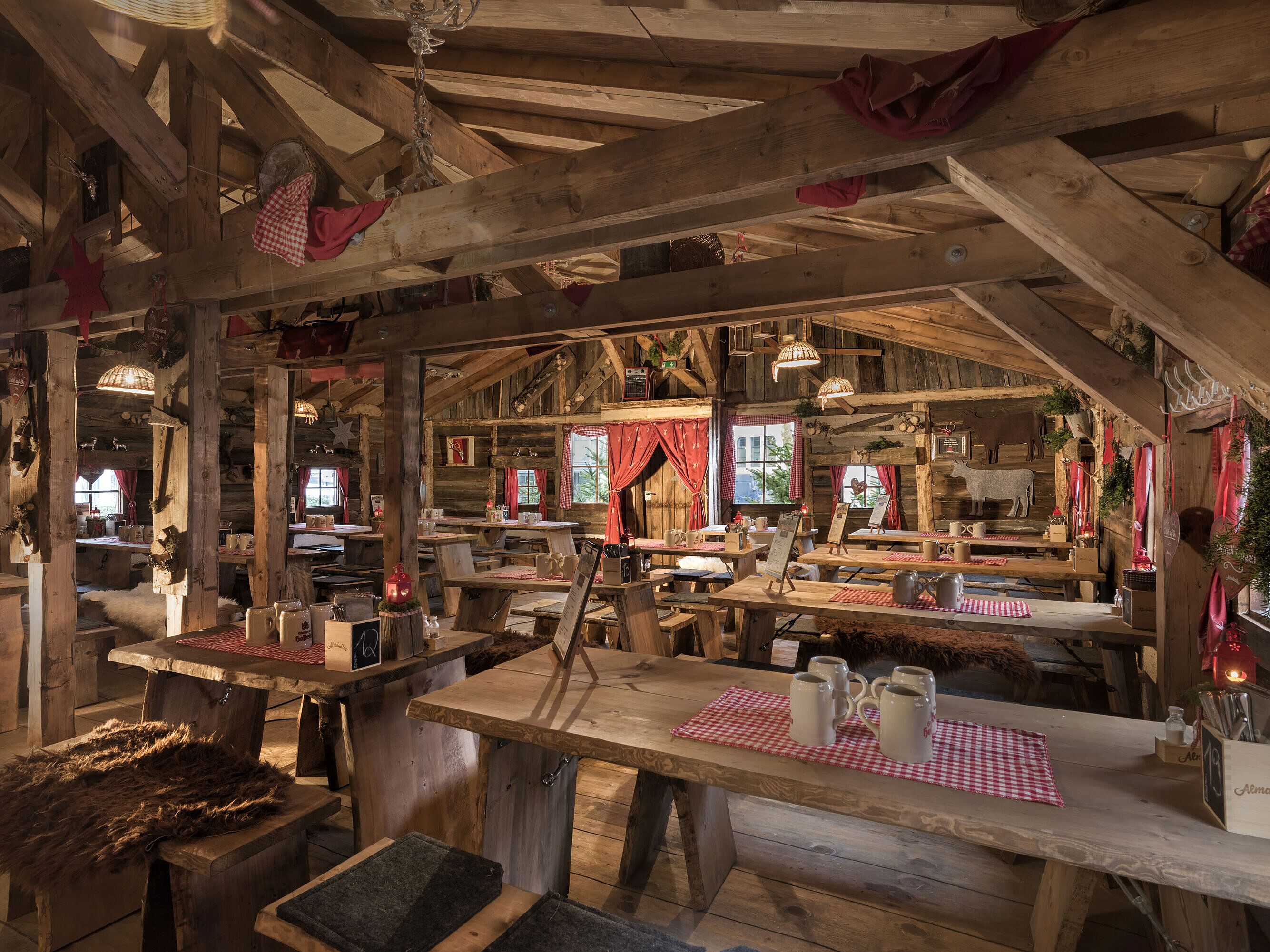 Warmer Innenbereich mit Holztischen, roten Vorhängen und uriger Deko in der Maritim Alm Stuttgart