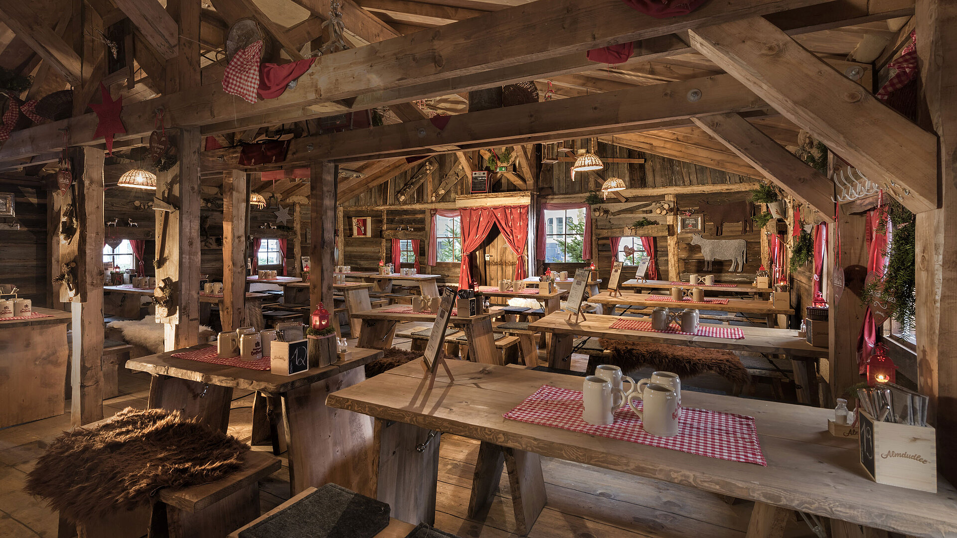 Warmer Innenbereich mit Holztischen, roten Vorhängen und uriger Deko in der Maritim Alm Stuttgart