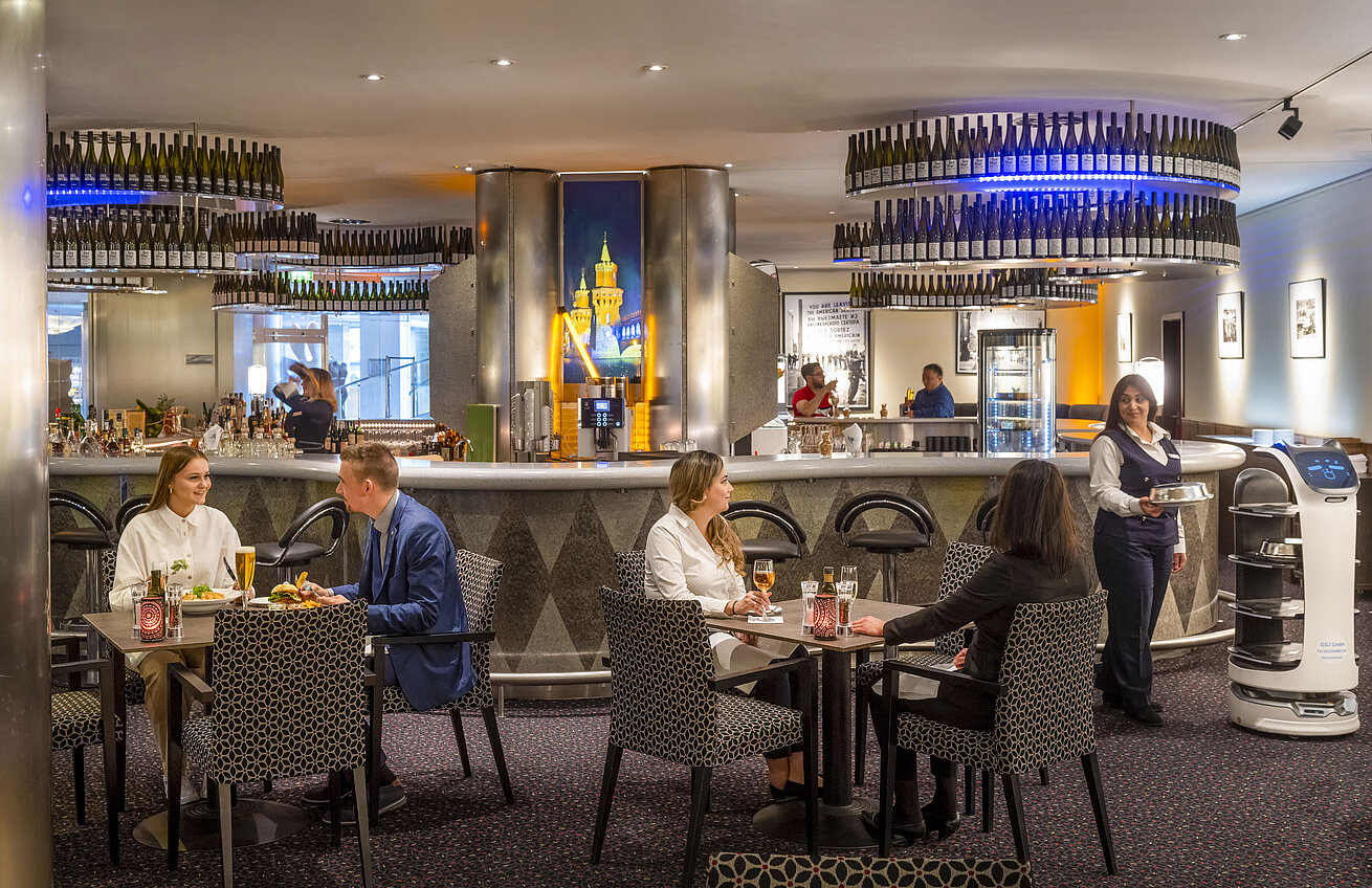 Gäste speisen in der Bar des Maritim proArte Hotel Berlin, umgeben von modernen Einrichtungen und einem Serviceroboter.