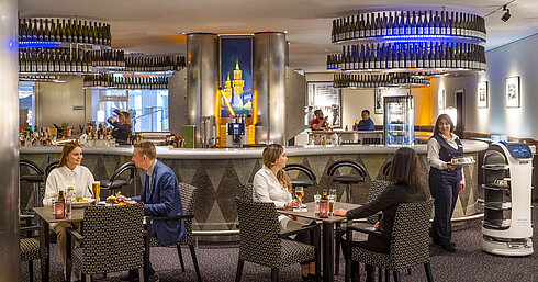 Gäste speisen in der Bar des Maritim proArte Hotel Berlin, umgeben von modernen Einrichtungen und einem Serviceroboter.