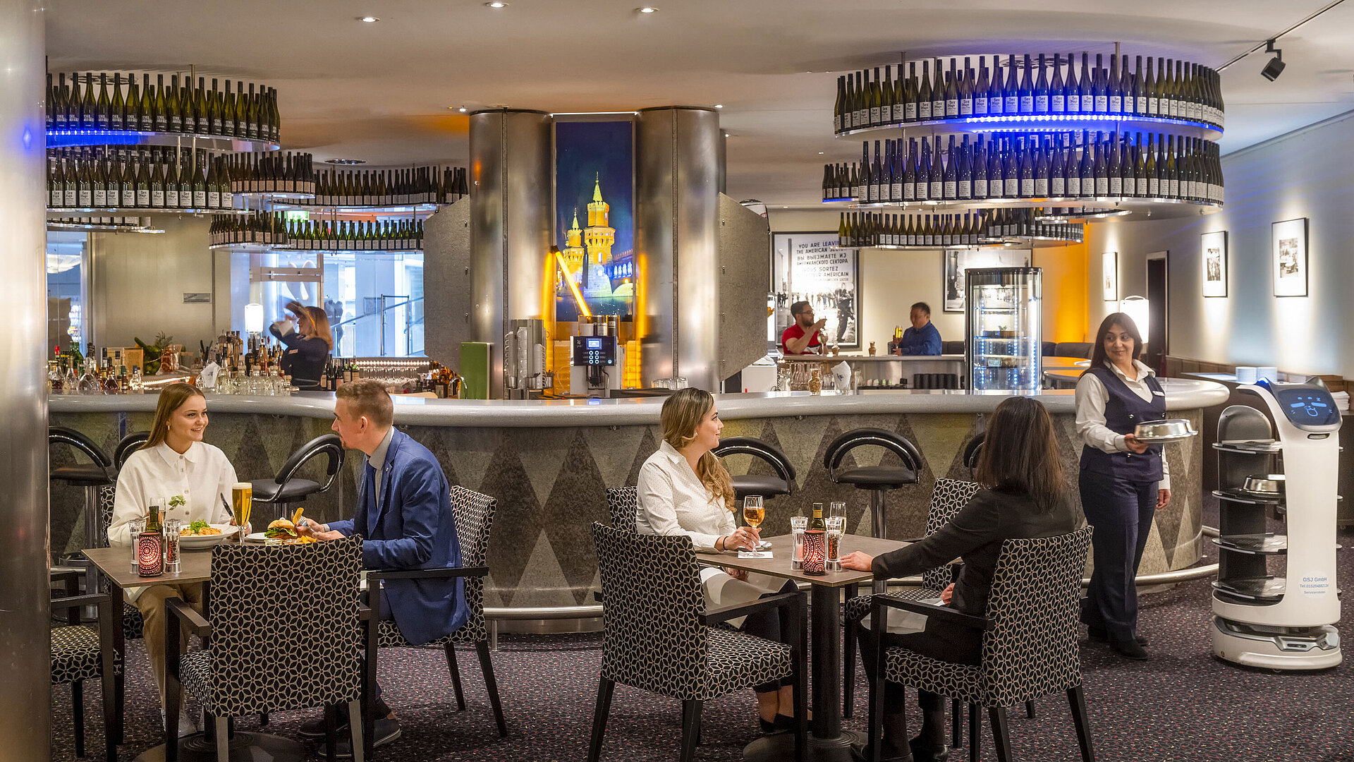 Gäste speisen in der Bar des Maritim proArte Hotel Berlin, umgeben von modernen Einrichtungen und einem Serviceroboter.