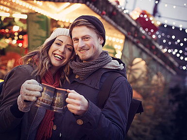 Paar stößt mit Glühwein auf einem festlich beleuchteten Weihnachtsmarkt an