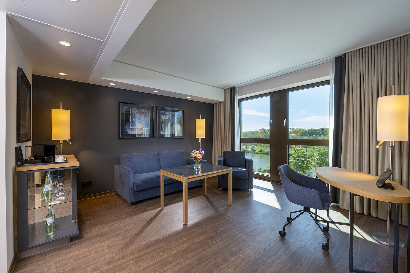 Helle Suite mit Sitzbereich, großem Fenster und Blick auf die Natur im Maritim Hotel Ingolstadt.
