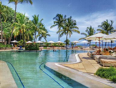 Großer Hotelpool mit Palmen, Sonnenliegen und Meerblick in tropischer Urlaubsatmosphäre