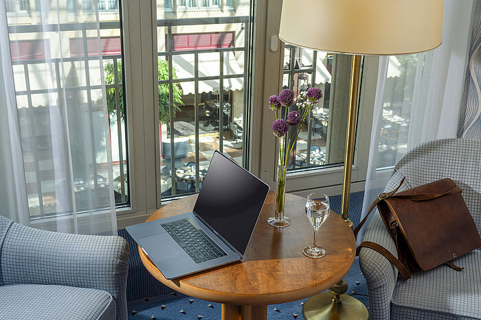 Classic Zimmer im Maritim Hotel Köln mit Laptop auf einem Tisch, Wasserglas, Ledertasche und Blumen in einer Vase.