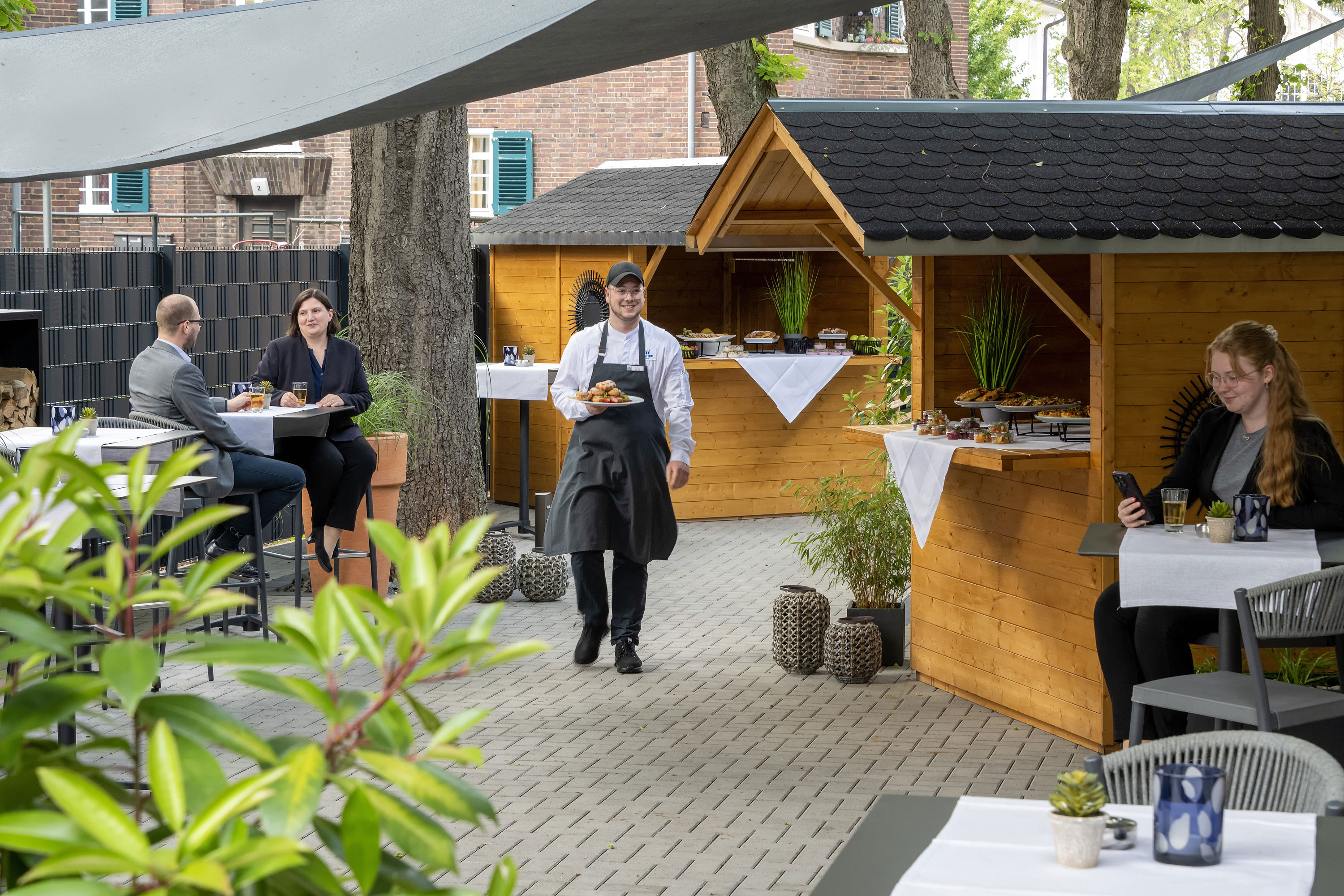 Außenterrasse Kellner serviert Speisen bei einer Veranstaltung auf der Terrasse des Maritim Hotel Darmstadt mit Holzhütten