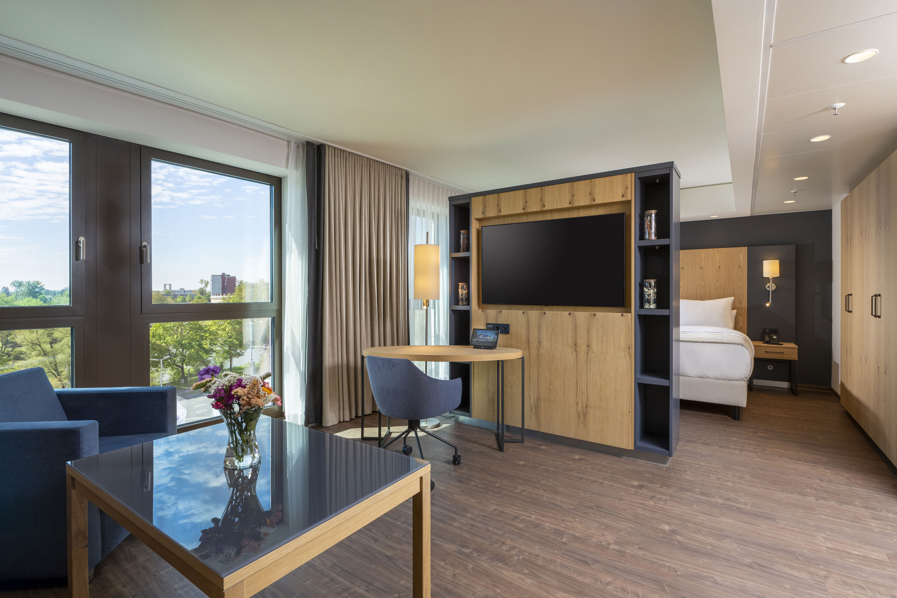 Helles Zimmer im Maritim Hotel Ingolstadt mit Sitzecke, Schreibtisch, großem TV und Blick auf die grüne Umgebung.