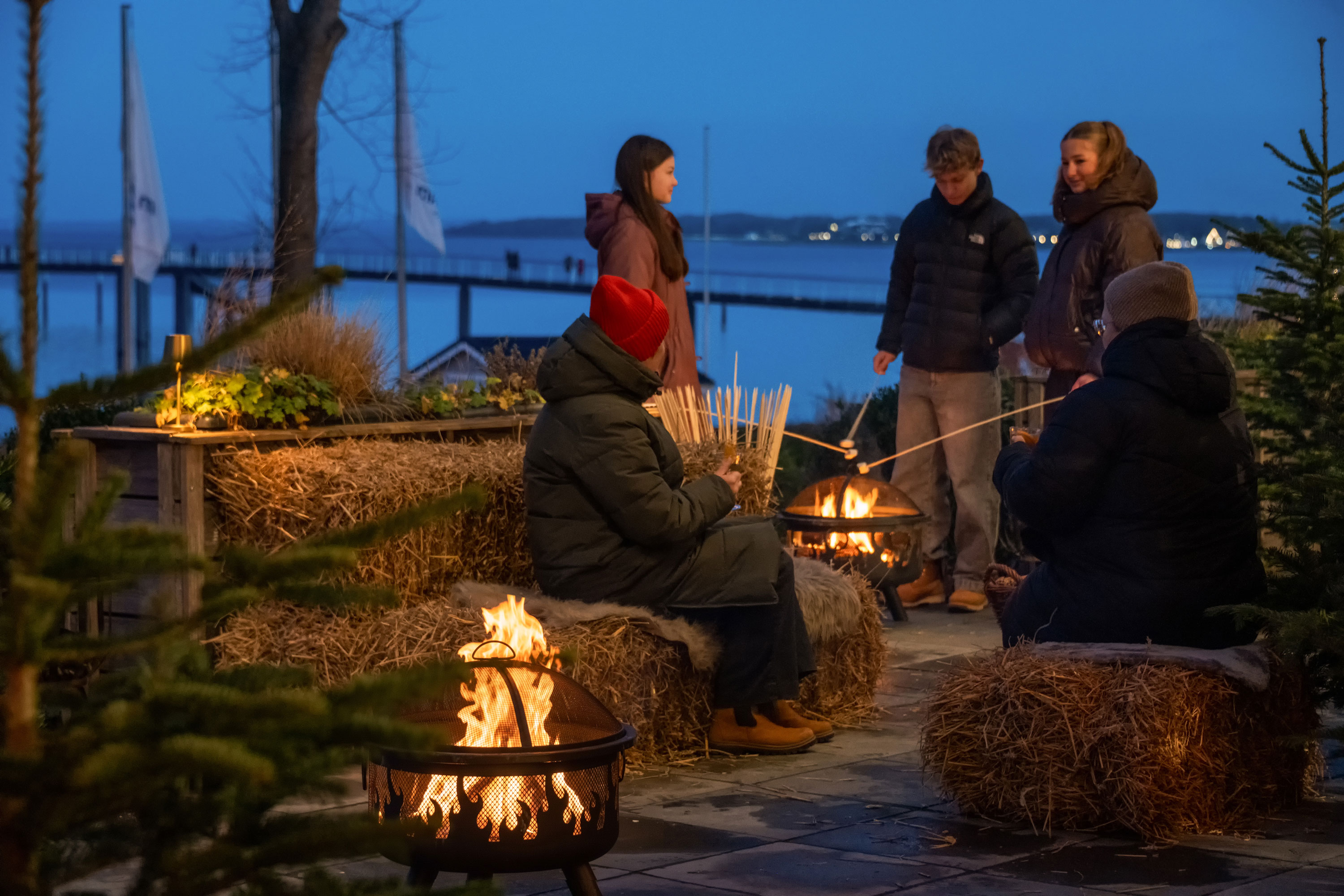 Winterzauber an der Ostsee Gäste genießen winterliche Atmosphäre am Feuerkorb auf einer festlich dekorierten Terrasse mit Ostseeblick.